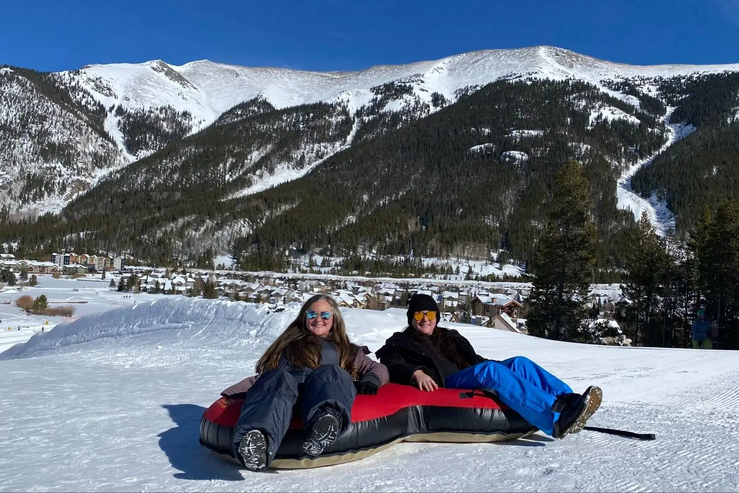 Mariya and Sam on a snow tube below a snowy mountain ridge