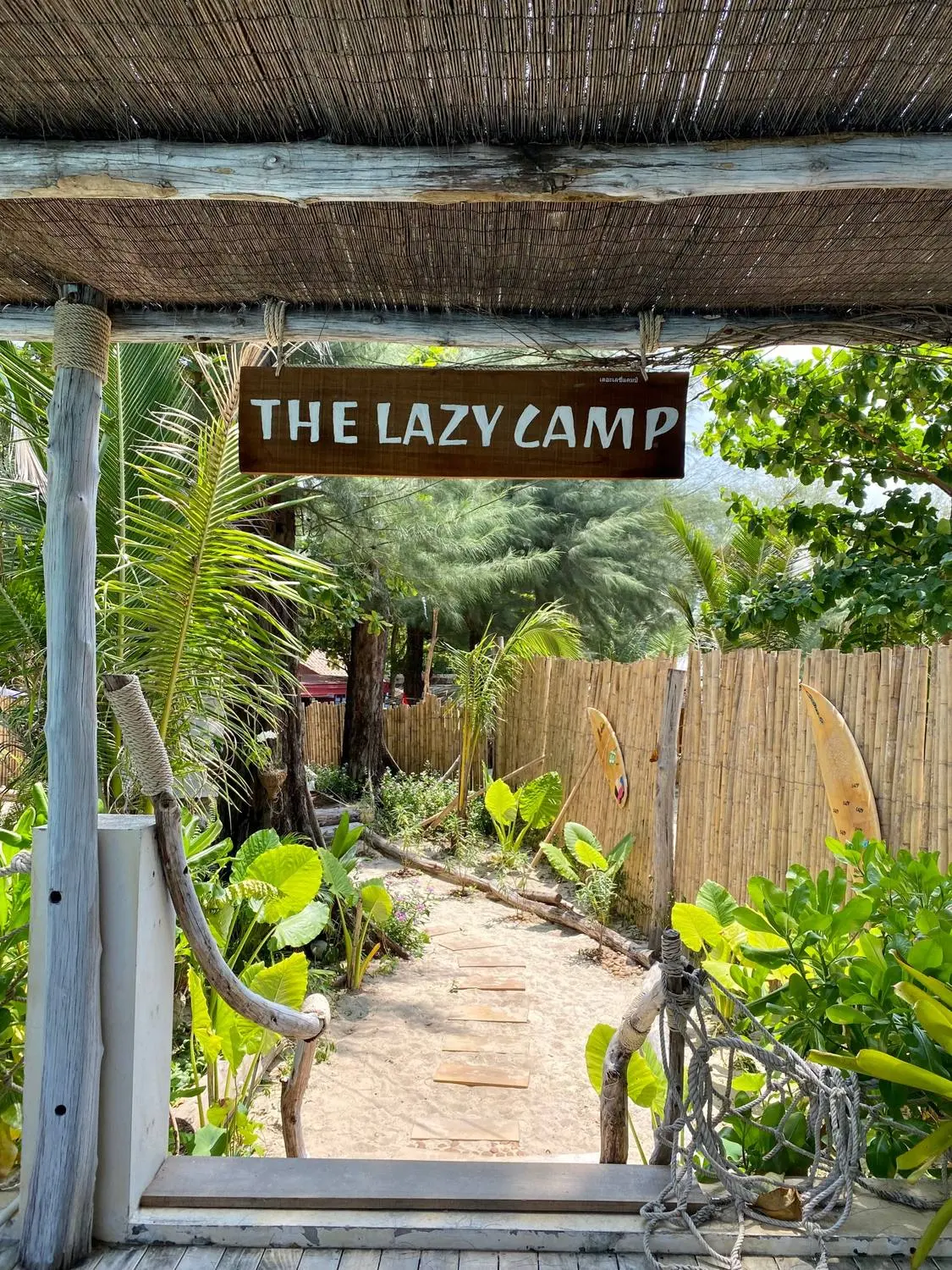 A garden path leading under a wooden sign that reads The Lazy Camp