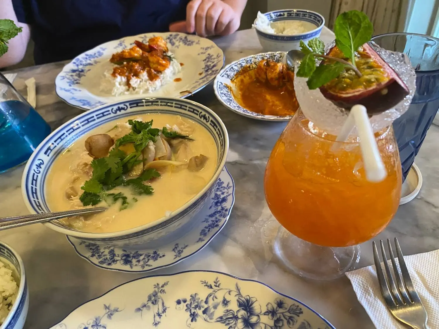 Lunch on a cafe table: a bowl of soup, plates of curry and an orange cocktail