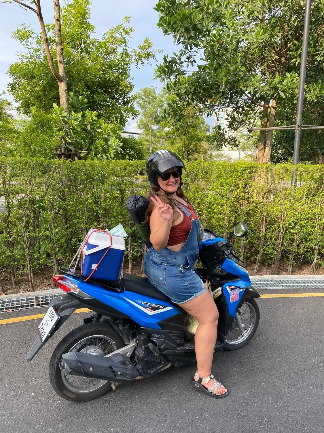 A woman in a helmet sitting on a blue scooter, waving