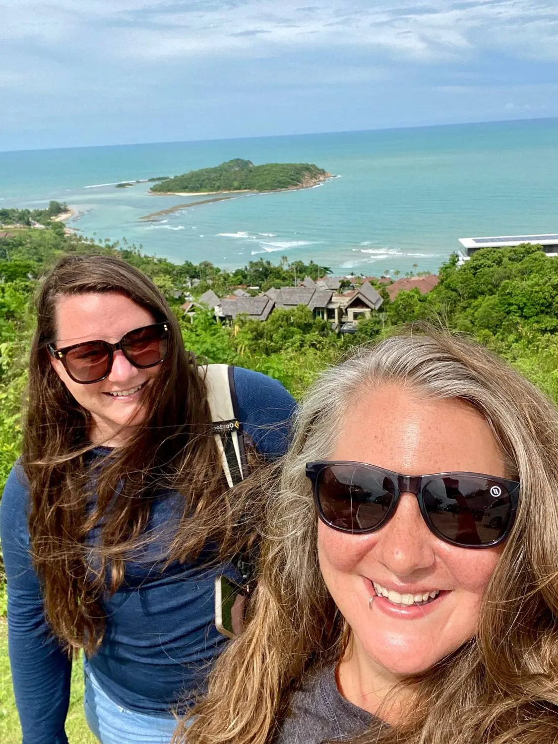 Mariya and Sam taking a selfie on a hilltop above the sea and a small island