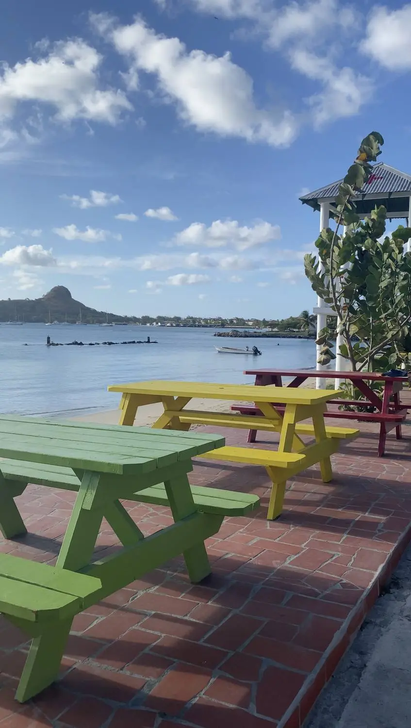 Colorful picnic tables on a waterfront terrace, a hill across the bay