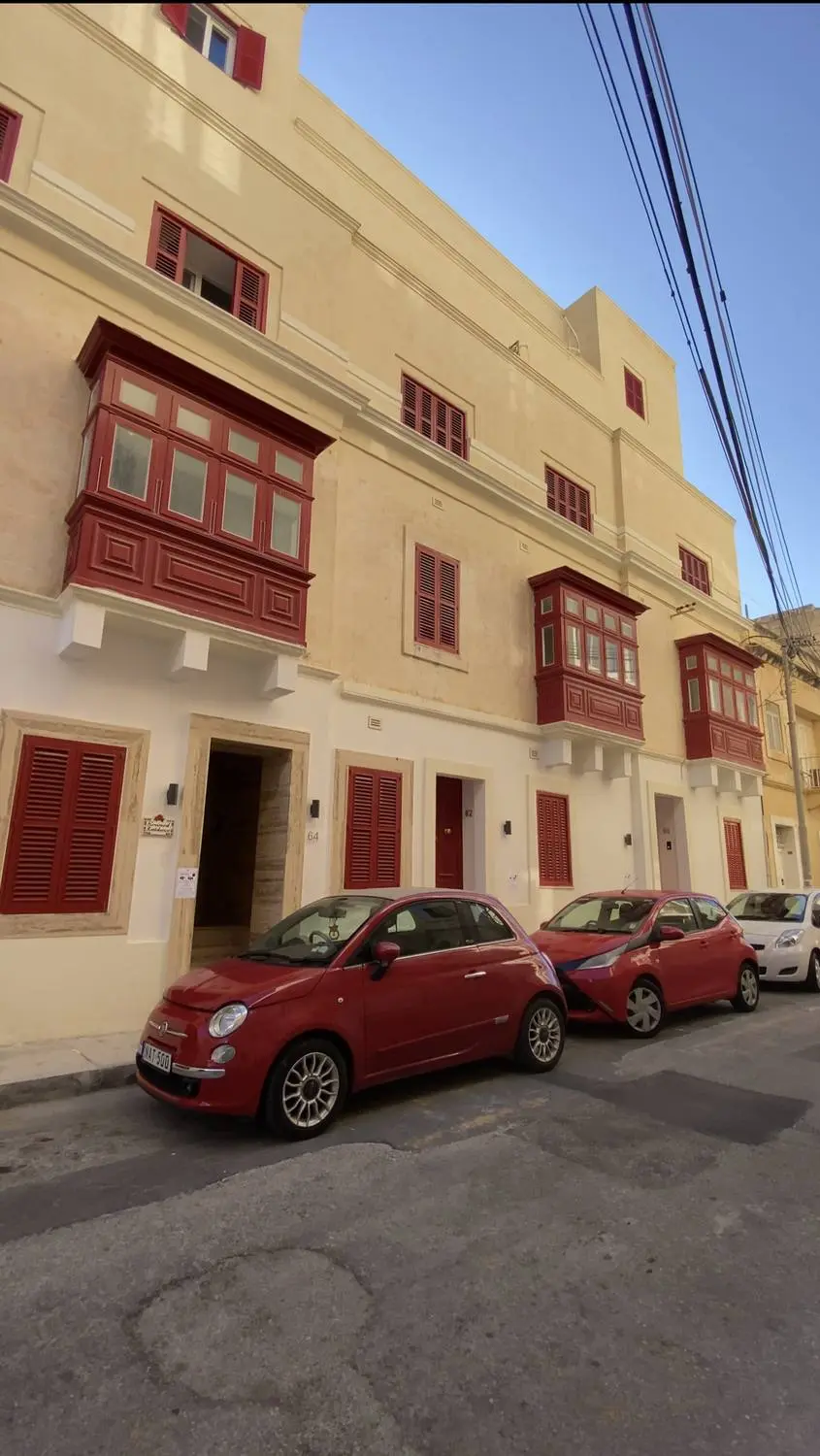 A cream stone street with red wooden balconies and small red cars parked below