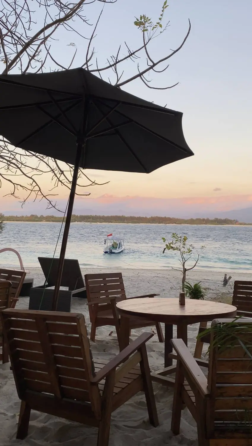 Beach chairs and a table under an umbrella on the sand at sunset