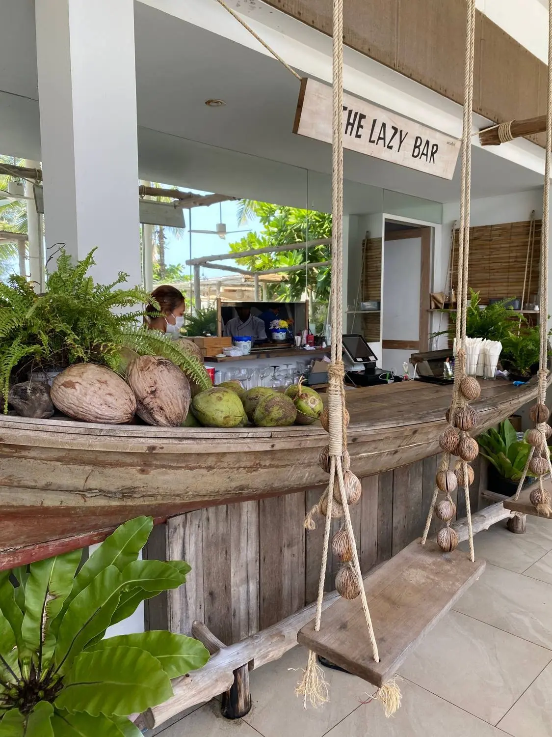 A beach bar called The Lazy Bar, with coconuts on the counter and rope swings for seats