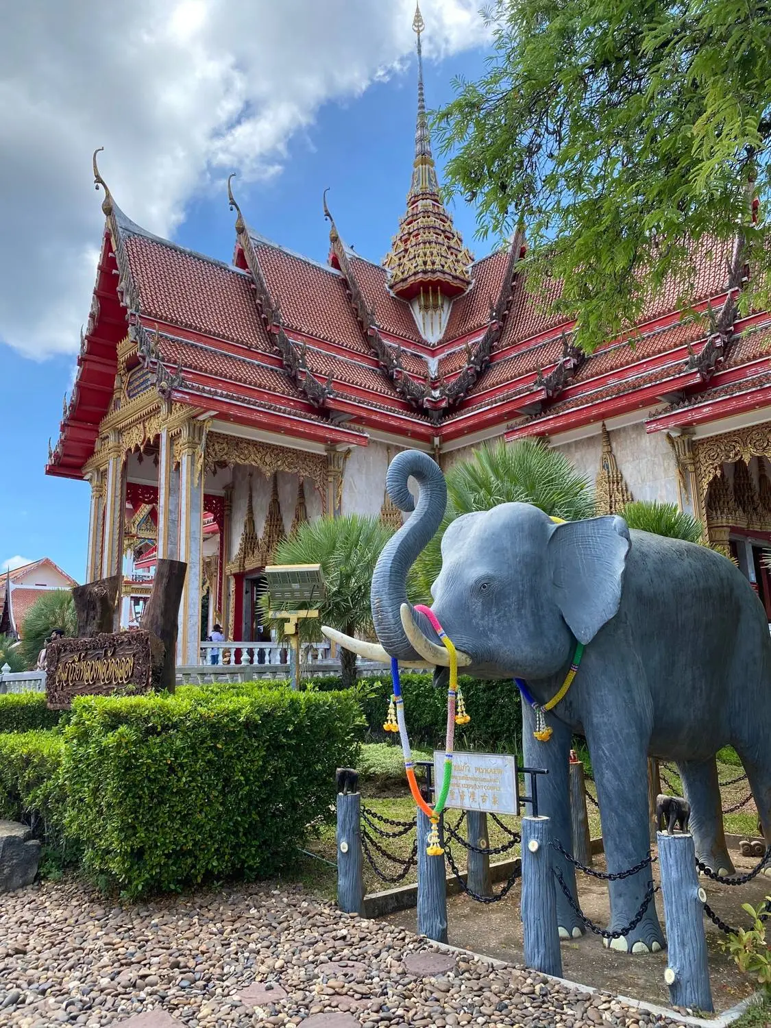 A statue of an elephant in front of an ornate red and gold Thai temple