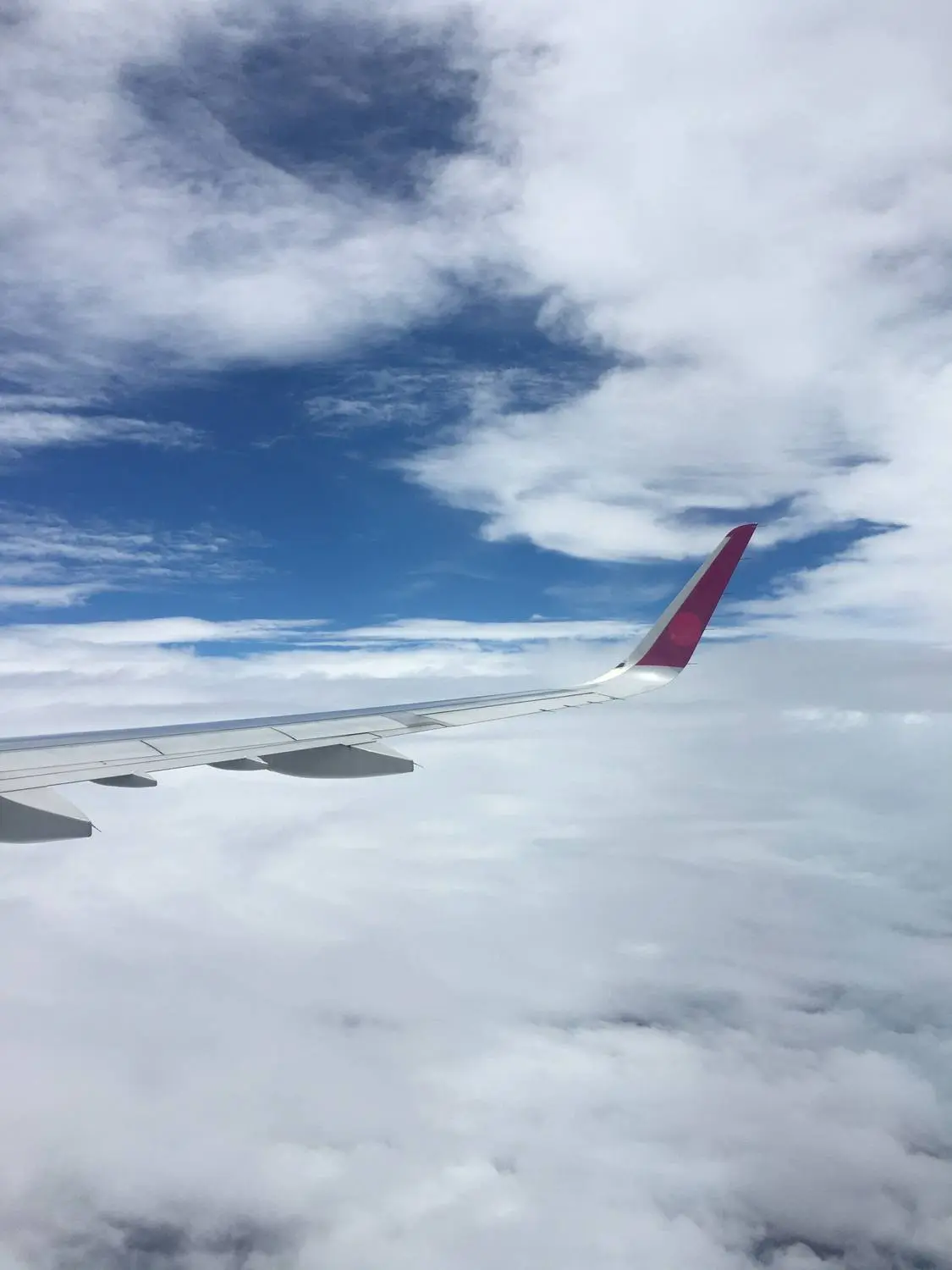 An airplane wing with a pink tip above white clouds