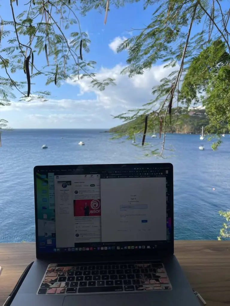 A laptop open on a table looking out over a bay with sailboats at anchor