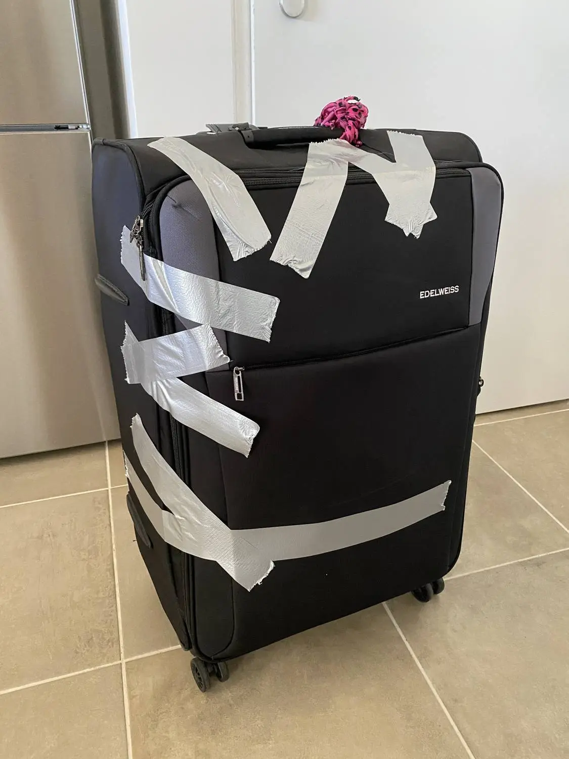 A black suitcase held together with strips of silver duct tape